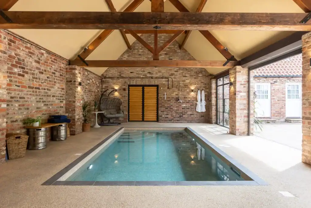 Indoor swimming pool with exposed brick walls and wooden beams in Yorkshire Escape.