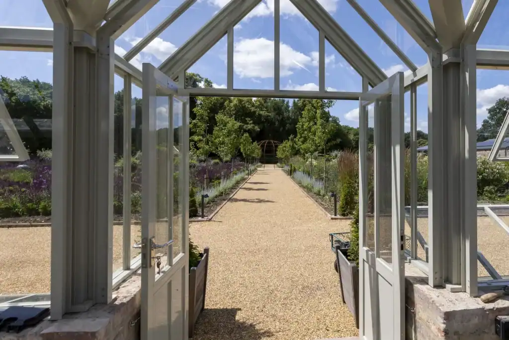 View through a glass greenhouse door onto a garden path with lush greenery.