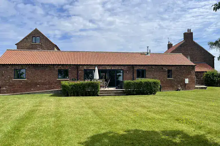 Traditional brick barn with red tiled roof and surrounding green lawn in Yorkshire.