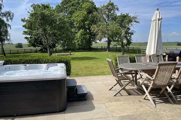 Outdoor patio with hot tub, dining table, and umbrella at The Dovecote Barn.