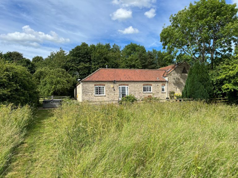 Stone cottage with red-tiled roof surrounded by greenery in Yorkshire.