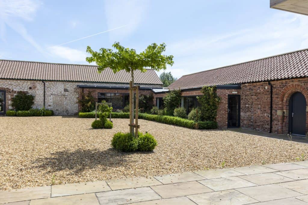 Charming courtyard at The Barn, Ganton with trees and brick buildings.