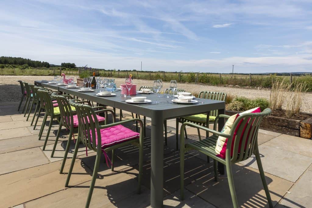 Outdoor dining table set with pink cushions in a rural Yorkshire setting.