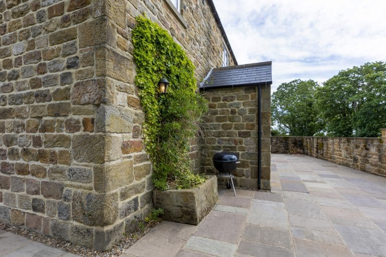 Stone wall with greenery and a small outdoor grill near Drovers Cottage.