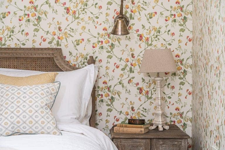 Cozy bedroom with floral wallpaper, wooden headboard, and vintage bedside lamp.