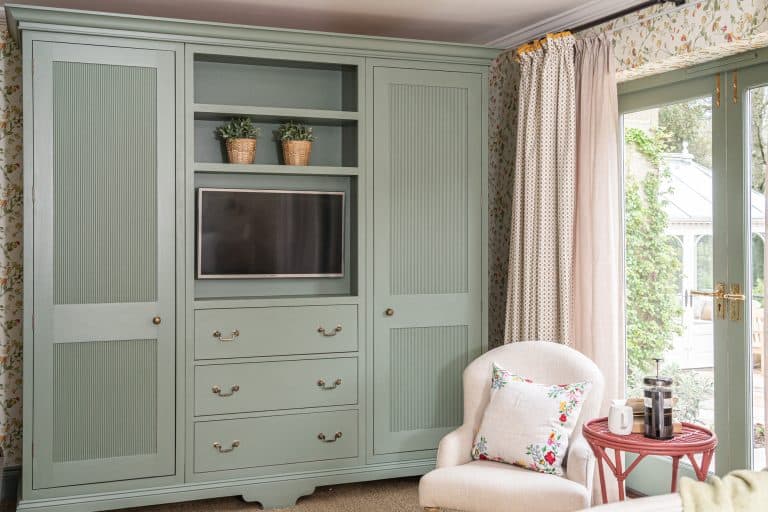 Cozy living room with built-in green wardrobe and a white armchair near a glass door.