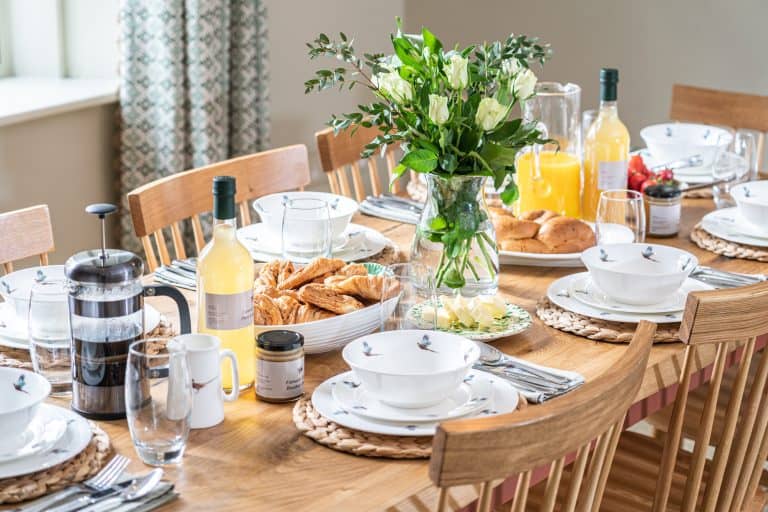 Elegant breakfast table set with flowers, croissants, and drinks in a bright dining room.