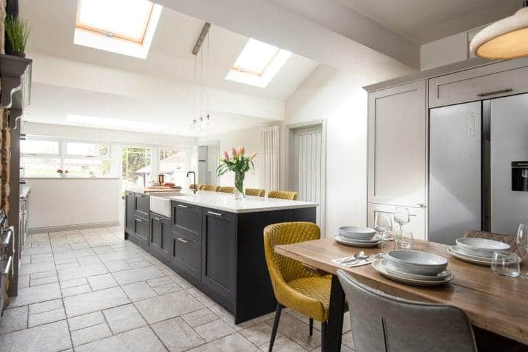 Modern kitchen with skylights, grey cabinets, and a dining area with yellow chairs.