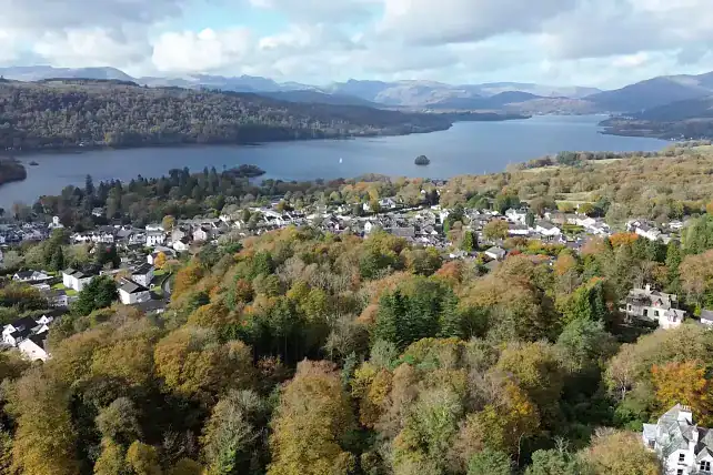 Aerial view of Windermere lake with surrounding autumnal trees and village.