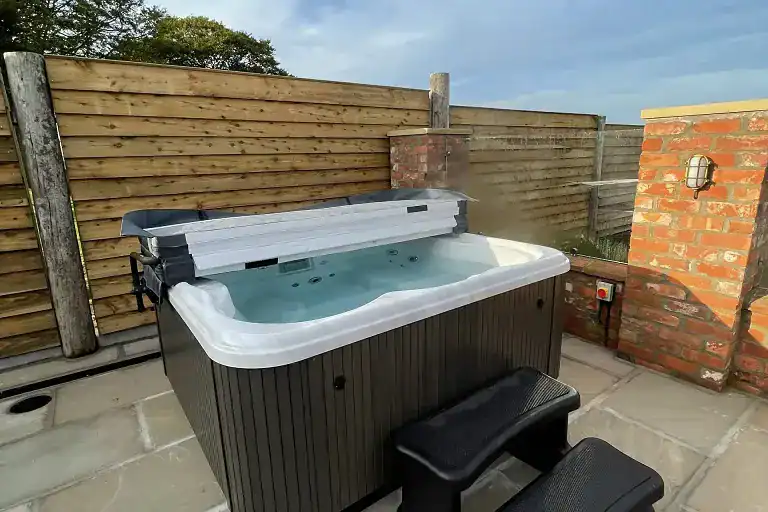 Hot tub on patio near Driffield with wooden fence and brick wall.