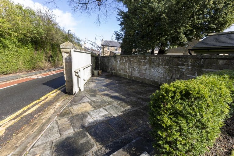 Stone-paved driveway with a white gate and surrounding greenery in Harrogate.