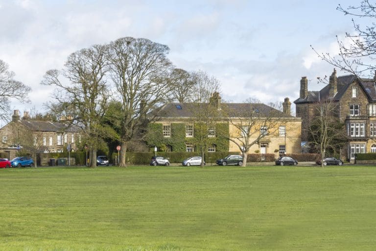 Historic buildings along Harrogate's scenic park with trees and parked cars.