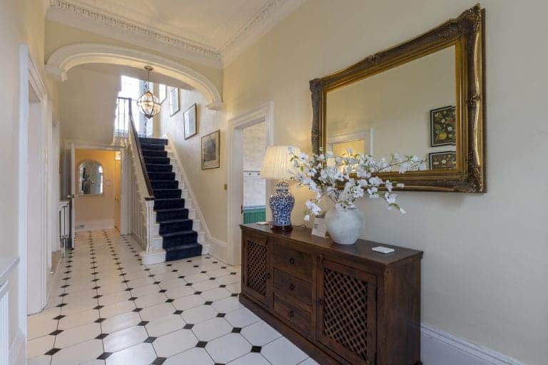 Elegant hallway with black and white tiled floor and a large mirror above a wooden sideboard.