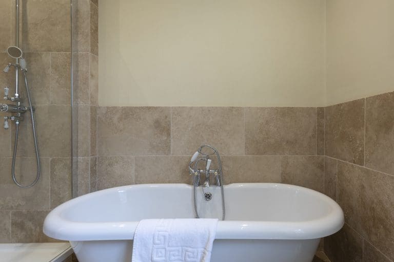 Elegant bathroom with a classic white bathtub and beige tiled walls.
