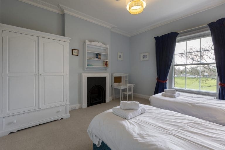 Spacious bedroom with two single beds, white wardrobe, and large window with dark curtains.