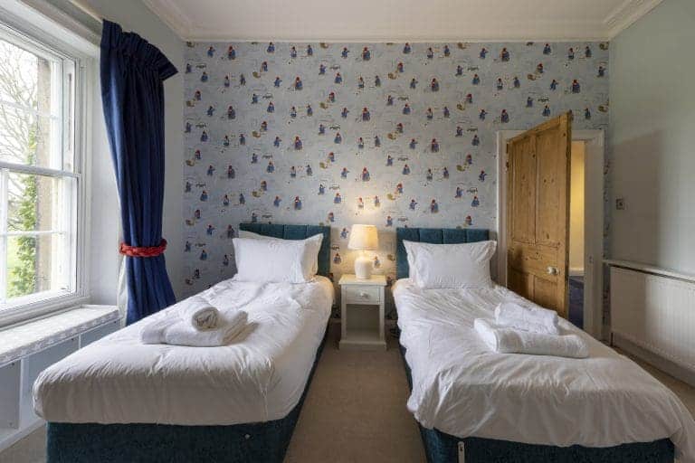 Twin bedroom in Granby House, Harrogate with colourful wallpaper and blue curtains.