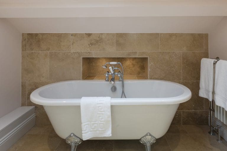 Elegant freestanding bathtub in a modern bathroom with beige tiled wall.