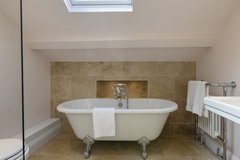 Elegant freestanding bathtub in a modern bathroom with skylight and beige tiles.