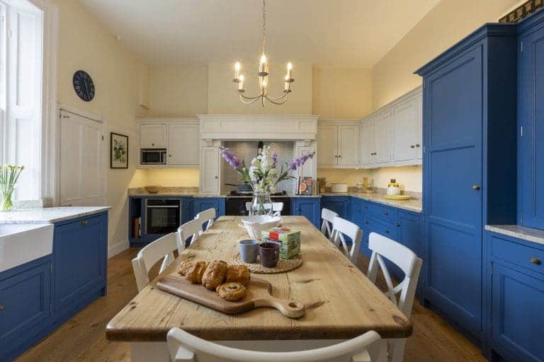 Modern kitchen with blue and white cabinetry and a wooden dining table.