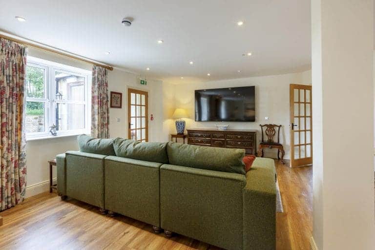 Cozy living room with green sofa, wooden flooring, and large TV in Yorkshire Dales cottage.