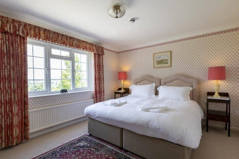 Cozy bedroom with large bed, floral curtains, and countryside view from window.