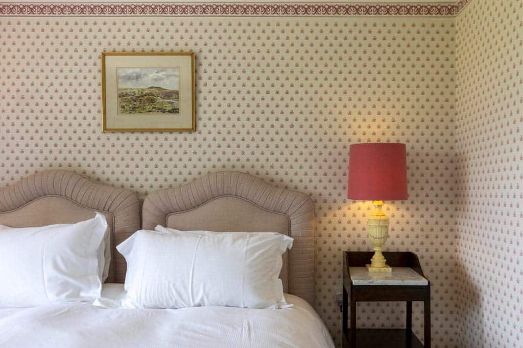Cozy bedroom with two beds, patterned wallpaper, and a bedside lamp.
