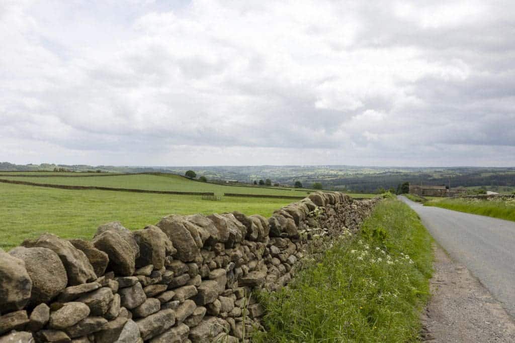 Scenic view of Yorkshire Dales with stone wall and country road under cloudy sky.