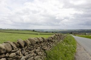 Scenic view of Yorkshire Dales with stone wall and country road under cloudy sky.