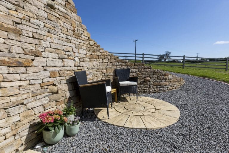 Outdoor seating area with two black chairs and potted plants by a stone wall.