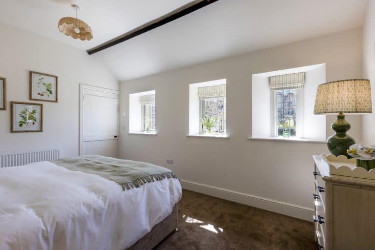 Bright bedroom with three windows and minimalist decor at Abbey Cottage.