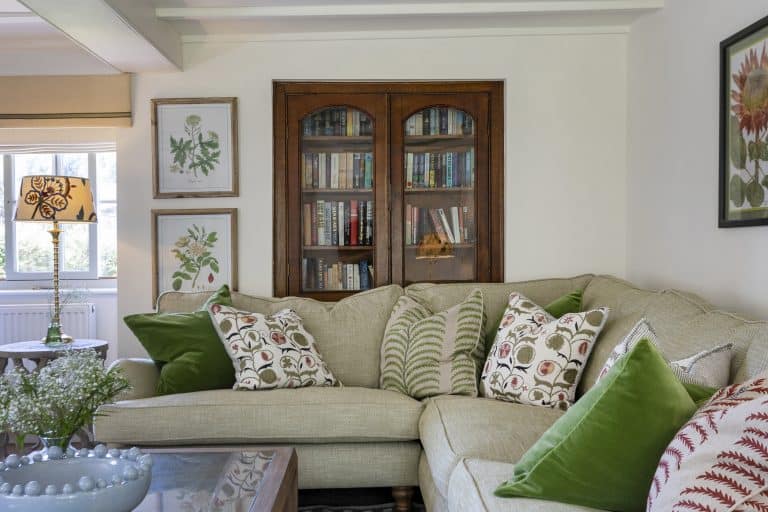 Cozy living room with beige sofa, green cushions, and wooden bookcase.