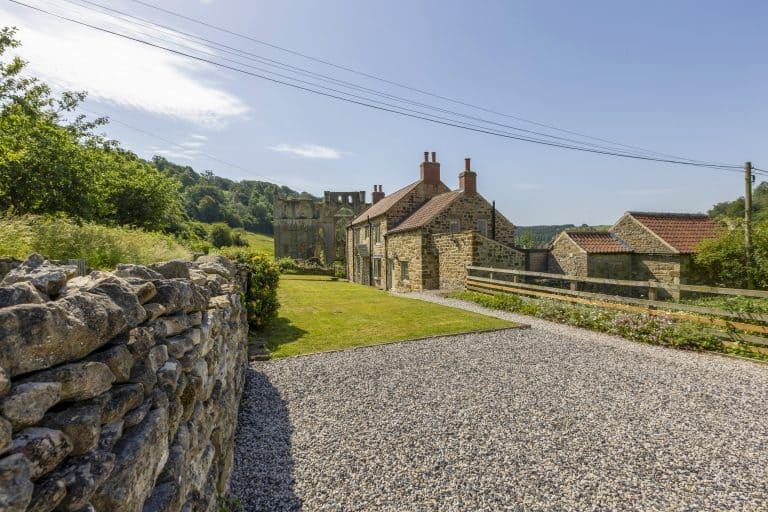 Historic stone cottage near Rievaulx Abbey with lush greenery and blue sky.
