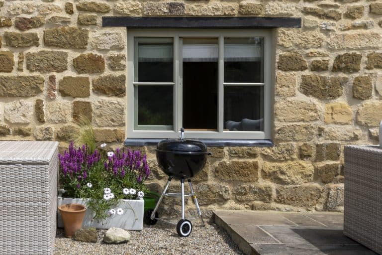 Stone cottage wall with window and outdoor barbecue grill.