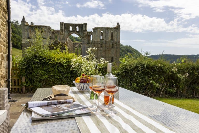 Outdoor dining table with wine glasses and a view of Rievaulx Abbey.