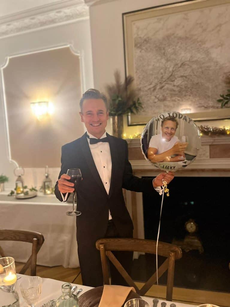 Man in tuxedo holding a glass of wine at birthday celebration.