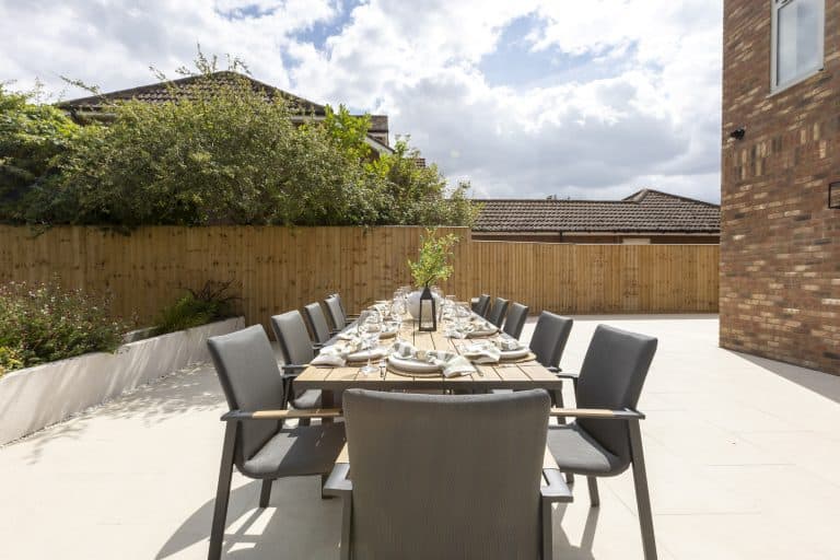 Outdoor dining area with a long table and grey chairs in a private garden.