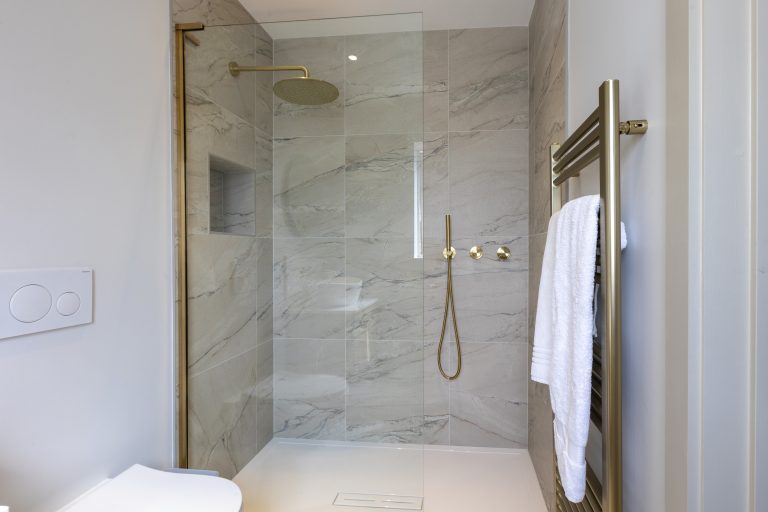 Modern walk-in shower with marble tiles and gold fixtures at Strathearn House near York.
