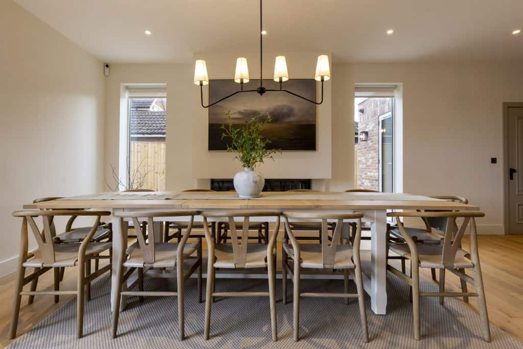 Modern dining room with large wooden table and eight chairs, chandelier overhead.