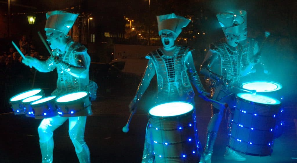 Performers in futuristic costumes playing drums at night in Yorkshire.